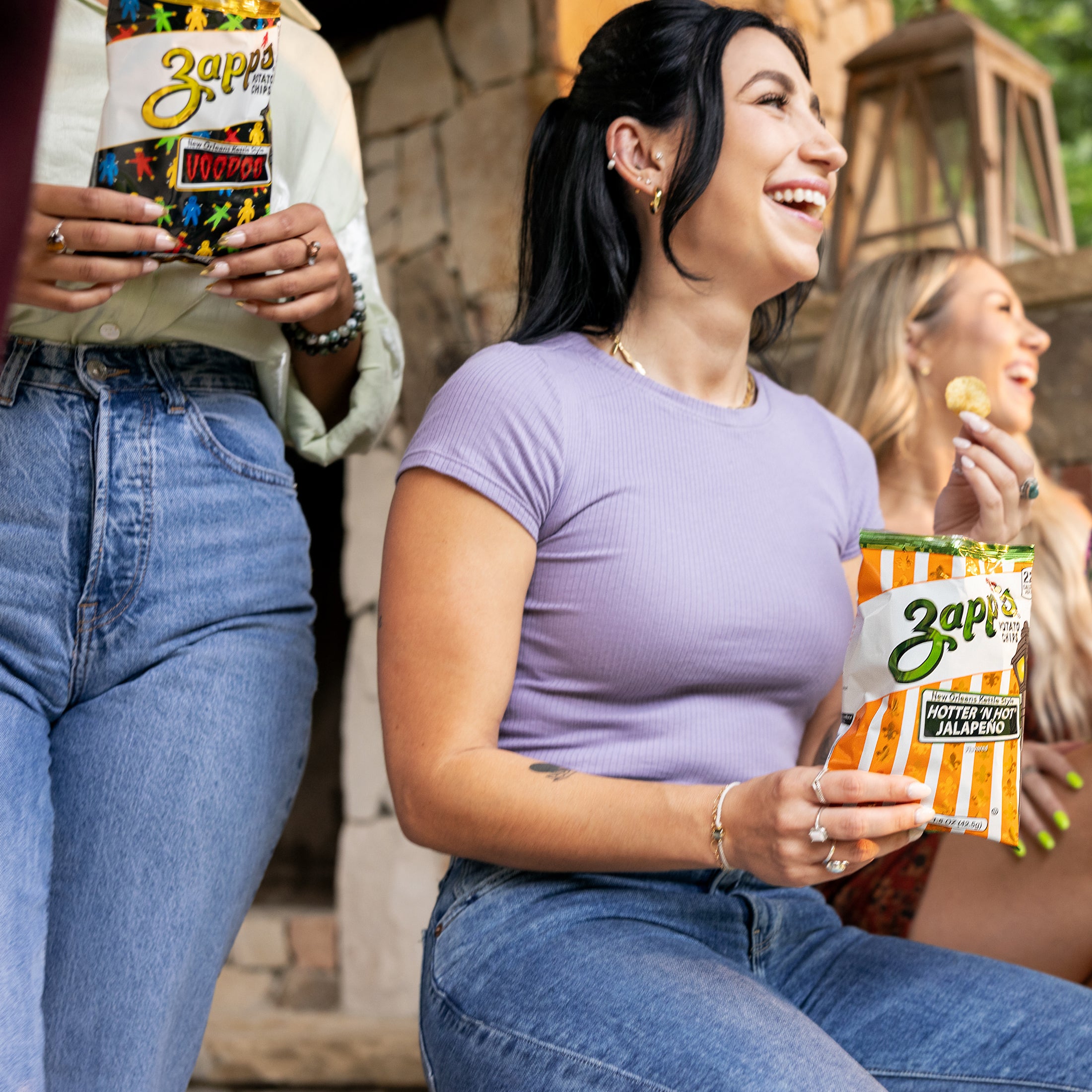 Woman holding a Zapps hot sauce packet outdoors with another person in the background.
